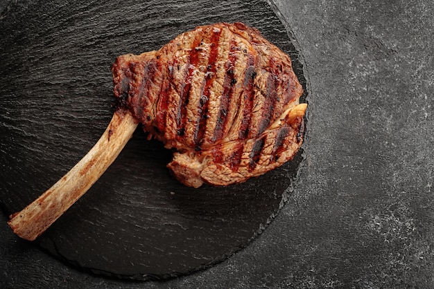 Foto gebratenes gegrilltes steak mit knochen auf einem schwarzen runden stein auf dunklem hintergrund
