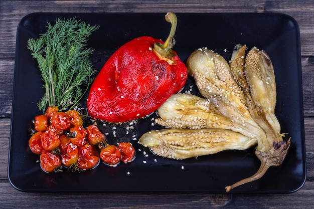 Gebratenes Gemüse, Auberginen und Paprika mit Tomaten auf schwarzem Teller aus nächster Nähe