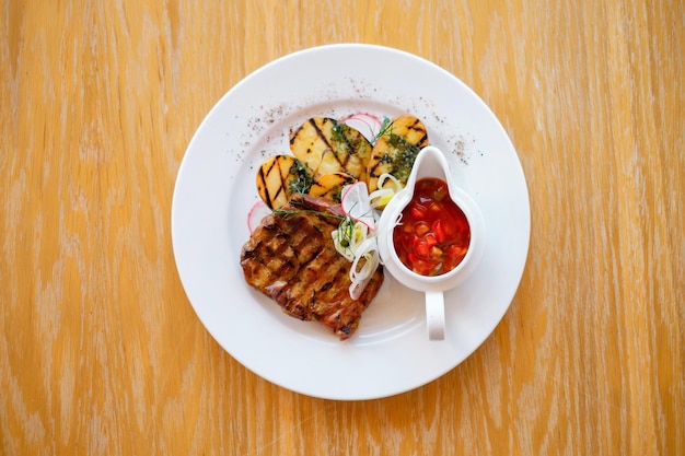 Gebratenes Grillfleisch auf einem weißen Teller mit Kartoffeln und Gemüse Gegrilltes BBQ mit Gemüse und Soße auf Holztisch und Pergamentpapier