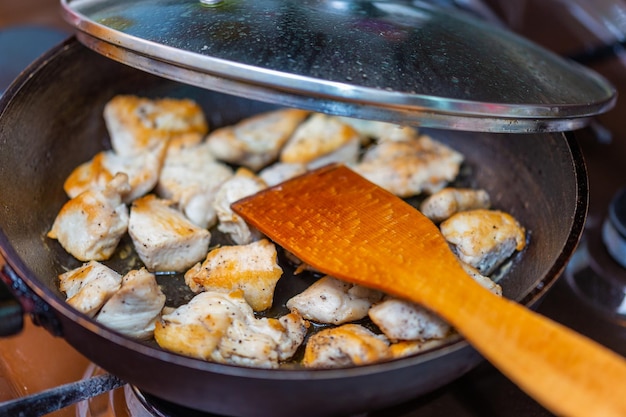 Gebratenes Hähnchen in einer offenen Pfanne mit gemahlenem schwarzem Pfeffer und Küchenspatel aus Holz