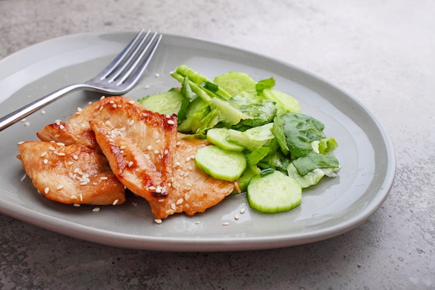 Gebratenes Hähnchenfilet in Sojasauce auf einem Teller mit Sesam und grünem Salat.