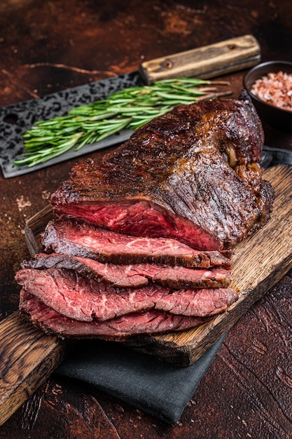 Foto gebratenes hängendes zartes oder in scheiben geschnittenes onglet-rindfleischsteak auf einem metzgerbrett mit hackmesser. dunkler hintergrund. ansicht von oben.