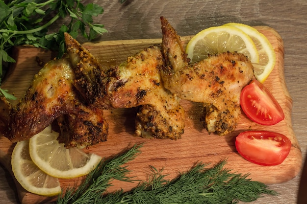 Gebratenes Hühnerflügel mit Tomate und Zitrone auf einem hölzernen Brett mit Petersilie und Dill