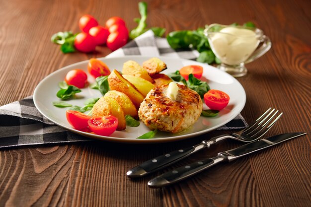 Gebratenes Hühnerschnitzel mit Kartoffelscheiben, serviert mit Tomaten-Kirsch-Mais-Salat. Traditionelles belorussisches Essen.