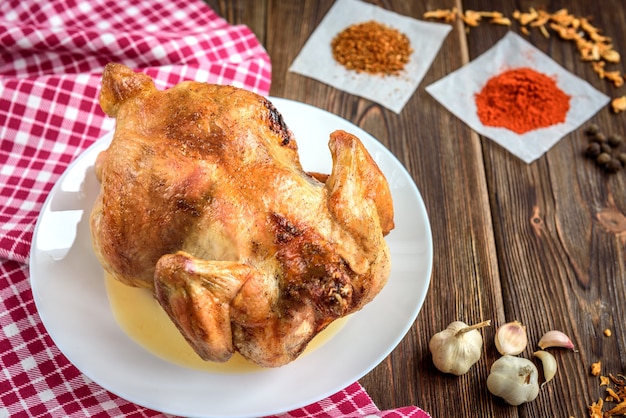 Gebratenes Huhn auf dunklem hölzernem Hintergrund mit Gewürzen und Knoblauch