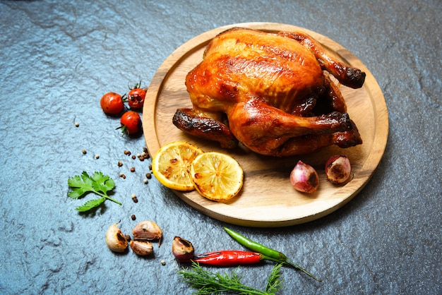 Gebratenes Huhn backte das vollständige Huhn, das mit Kräutern und Gewürzen auf hölzerner Platte und Dunkelheit gegrillt wurde