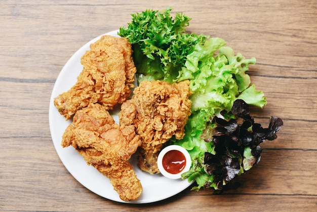 Gebratenes Huhn knusperig auf weißer Platte mit Ketschup- und Salatkopfsalatgemüse auf Holz