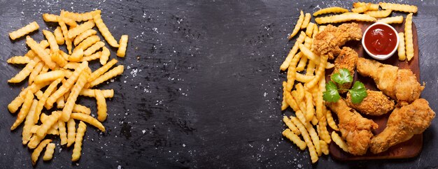 Gebratenes Huhn und Pommes Frites auf einem dunklen Tisch, Draufsicht