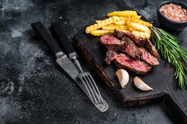 Gebratenes in Scheiben geschnittenes Machetenrock-Rindfleischsteak auf Holzbrett mit Pommes frites