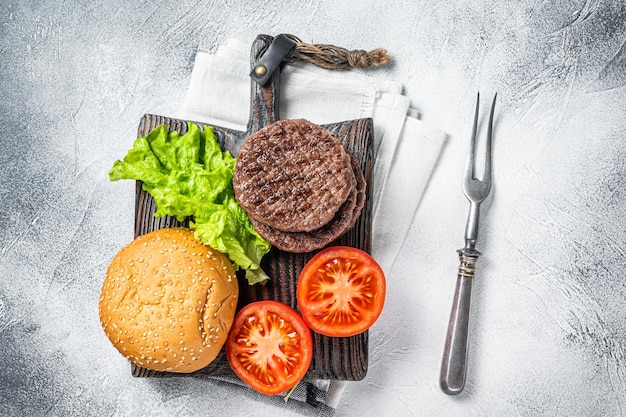 Gebratenes Kotelett für Burger mit Gemüse und Gewürzen auf Holzbrett Weißer Hintergrund Ansicht von oben