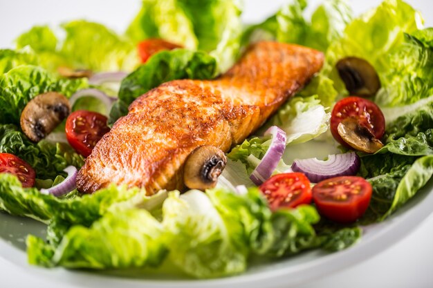 Gebratenes Lachsfilet mit frischem Gemüsesalat auf weißem Teller.