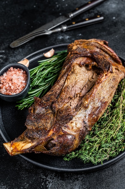 Gebratenes Lamm Hammelschulterfleisch auf einem Teller mit Messer und Gabel. Schwarzer Hintergrund. Ansicht von oben.