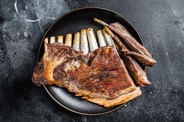 Gebratenes Lammkarree Rippchen Hammel Spareribs geschnittenes Fleisch auf Platte Schwarzer Hintergrund Ansicht von oben