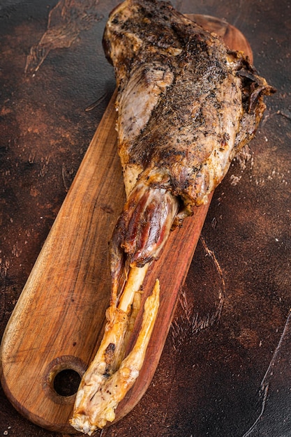 Gebratenes Lammkeulenfleisch mit Kräutern und Gewürzen auf einem Schneidebrett Dunkler Hintergrund Draufsicht