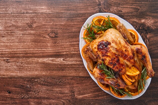 Gebratenes oder gebackenes ganzes Huhn mit Rosmarin und Orangen, hausgemacht für traditionelles Weihnachtsessen auf einem alten rustikalen Holztisch. Draufsicht mit Kopienraum.