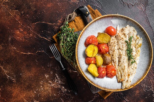 Gebratenes Pollock-Fischfilet in Platte mit Beilage Tomate und Kartoffel Dunkler Hintergrund Ansicht von oben Kopieren Sie Platz