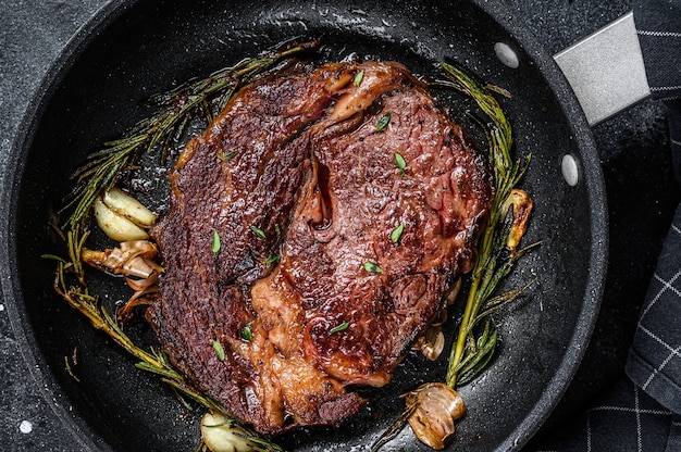 Gebratenes Rib-Eye-Steak, Rib-Eye-Rindfleisch in einer Pfanne. Schwarzer Hintergrund. Ansicht von oben.