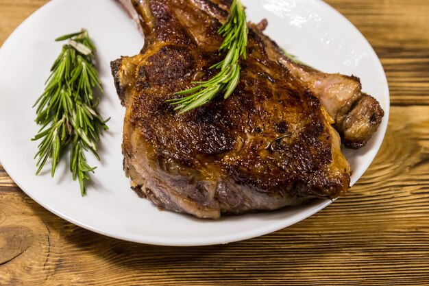 Gebratenes Rindersteak am Knochen mit Rosmarin in weißer Platte auf Holztisch