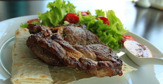 Gebratenes Rindfleisch mit Gemüse, roter Soße und Pita auf weißer Platte