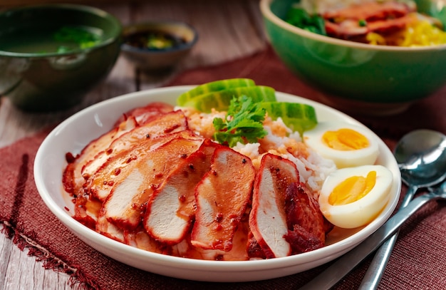 Foto gebratenes rotes schweinefleisch mit reis und eiernudeln in einer grünen schüssel, die mit gekochtem ei serviert wird