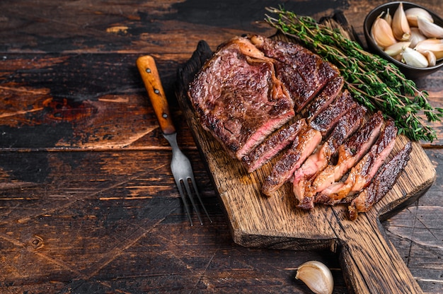 Gebratenes und geschnittenes Rib-Eye-Rinderfleischsteak auf einem hölzernen Schneidebrett mit Thymian