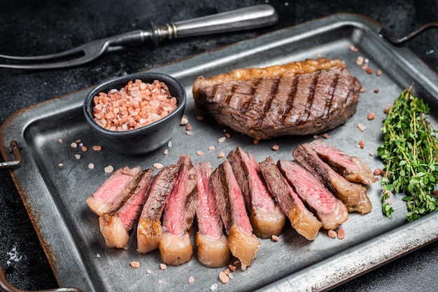 Gebratenes und in Scheiben geschnittenes Top Sirloin Steak Gegrilltes Cup Rump Beef Steak auf einem Serviertablett aus Stahl mit Gewürzen Schwarzer Hintergrund Ansicht von oben