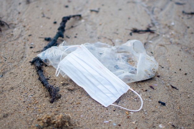 Gebrauchte Gesichtsmaske und Plastikmüll im Sand des Strandes