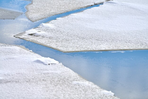 Gebrochenes Eis des gefrorenen Flusses mit weißem Schnee oben und blauem Wasser unten. Eis Textur Hintergrund, Nahaufnahme.