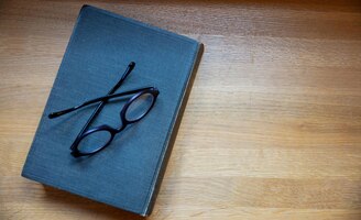 Gebundenes notizbuch auf einem tisch geschlossenes altes schwarzes buch und brillen auf draufsicht des hölzernen hintergrundes