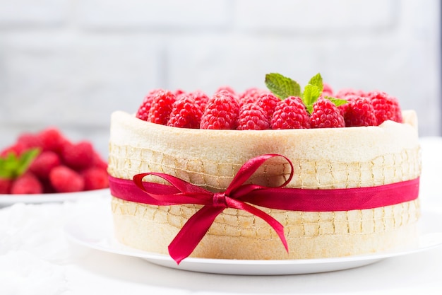 Geburtstag Biskuit mit Himbeeren verziert weißes Band und Bogen auf einem hellen Hintergrund