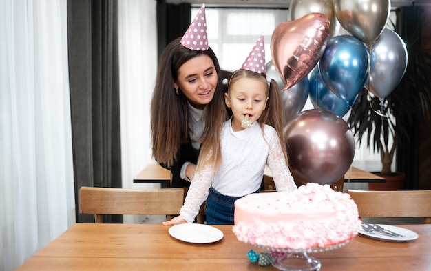 Geburtstag mutter und tochter in hüten feiern auf dem tisch einen festlichen kuchen und luftballons.