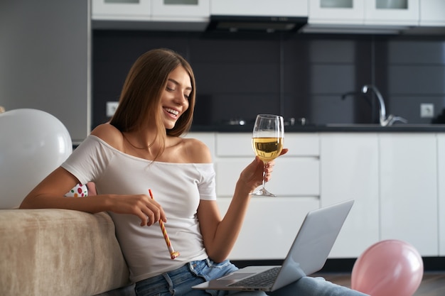 Geburtstagsfrau mit Glas Wein beim Videoanruf zu Hause