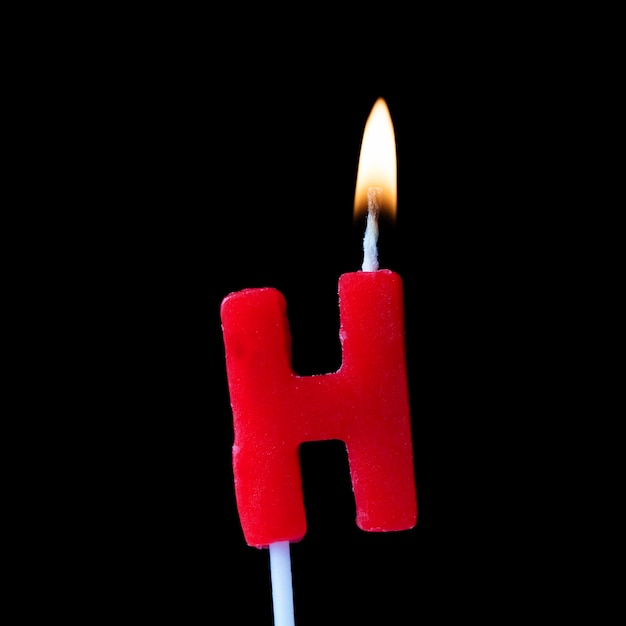 Geburtstagskerze zur Feier des Buchstaben H vor schwarzem Hintergrund
