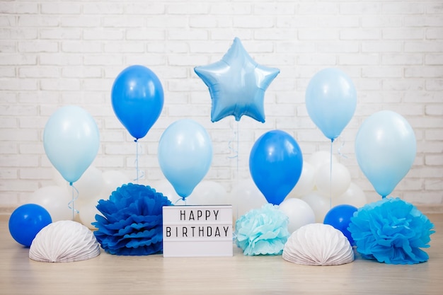 Geburtstagsparty-Dekoration, Luftballons, Papierbälle und Leuchtkasten mit Happy Birthday-Text über einer Ziegelwand