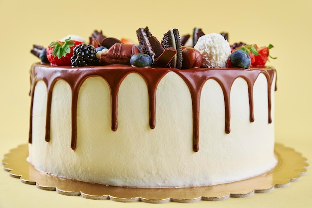 Geburtstagstorte auf gelbem Hintergrund. Nahaufnahme von Kuchen dekoriert mit frischen Beeren und Schokolade