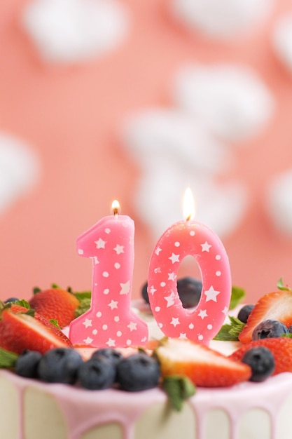Geburtstagstorte Nummer 10 Schöne rosa Kerze im Kuchen auf rosa Hintergrund mit weißen Wolken Closeup und vertikale Ansicht