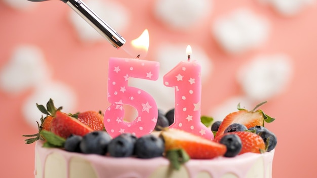 Geburtstagstorte Nummer 51 rosa Kerze auf schönem Kuchen mit Beeren und Feuerzeug mit Feuer vor dem Hintergrund von weißen Wolken und rosa Himmel Detailansicht