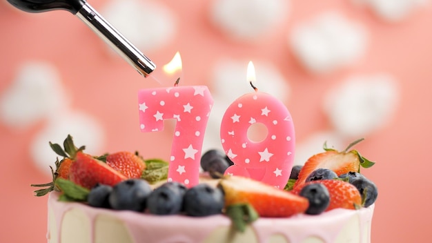 Foto geburtstagstorte nummer 79 rosa kerze auf schönem kuchen mit beeren und feuerzeug mit feuer vor dem hintergrund von weißen wolken und rosa himmel detailansicht