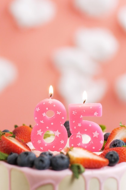 Foto geburtstagstorte nummer 85 schöne rosa kerze im kuchen auf rosa hintergrund mit weißen wolken nahaufnahme und vertikale ansicht