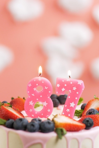 Geburtstagstorte Nummer 87 Schöne rosa Kerze im Kuchen auf rosa Hintergrund mit weißen Wolken Closeup und vertikale Ansicht