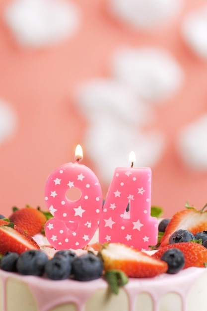 Geburtstagstorte Nummer 94 Schöne rosa Kerze im Kuchen auf rosa Hintergrund mit weißen Wolken Closeup und vertikale Ansicht