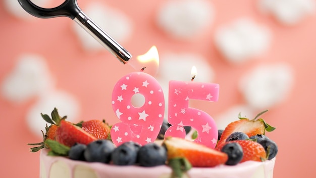 Geburtstagstorte Nummer 95 rosa Kerze auf schönem Kuchen mit Beeren und Feuerzeug mit Feuer vor dem Hintergrund von weißen Wolken und rosa Himmel Detailansicht