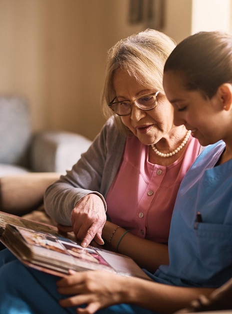 Foto gedächtnisübungen sind sehr wichtig für ihre gesundheit aufnahme einer krankenschwester und einer seniorin, die gemeinsam ein fotoalbum betrachten