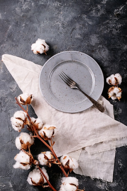 Gedeck für das Abendessen. Eine blaue moderne Keramikplatte mit silberner Gabel verziert mit Baumwollblume über dunkler Texturoberfläche. Draufsicht, flach liegen.