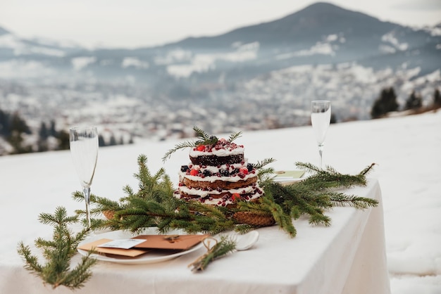Gedeckter Tisch mit Kuchen für zwei Verliebte in den Bergen. Wunderschöne Hochzeitsdeko im Winterstil vor dem Hintergrund der Berge.