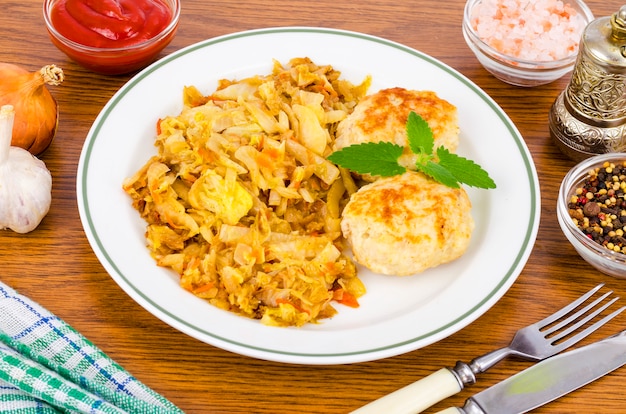 Gedünsteter kohl, fleischkoteletts, gewürze, salz auf holztisch.