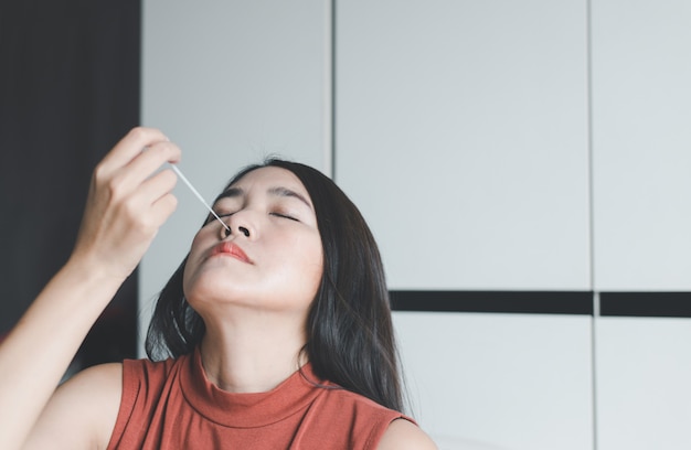 Geduldige asiatische Frau, die einen Nasenabstrich-Selbsttest-Antigen-Schnelltest-Kit zur Überprüfung eines Covid-19 zu Hause durchführt