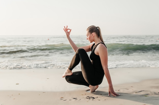 Geeignete Frau der Junge üben Yoga asana auf dem Sand nahe Ozean