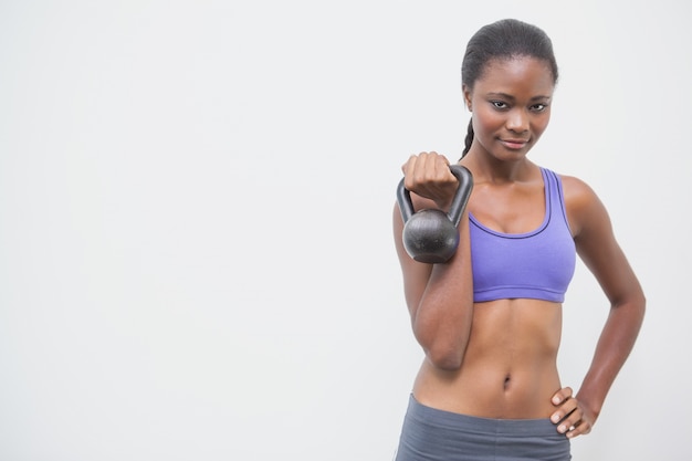 Geeignete Frau, die an der Kamera hält kettlebell lächelt