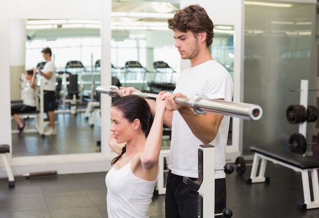 Geeignete Frau, die Barbell mit ihrer Traineraufstellung anhebt